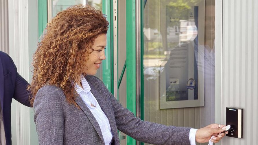 Una mujer sostiene un soporte de identificación delante de un lector de control de acceso para abrir la puerta.