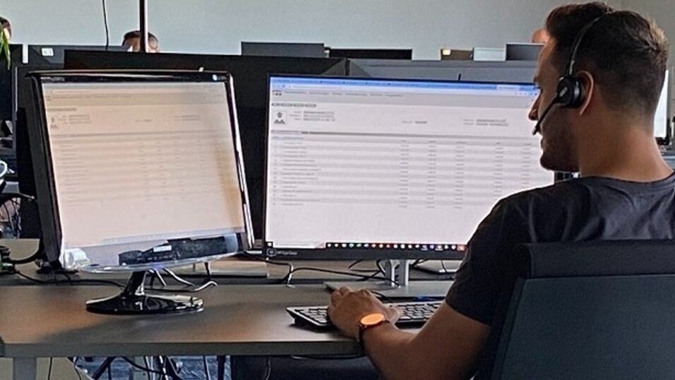 Hombre sentado con auriculares en la oficina frente a dos pantallas de PC.