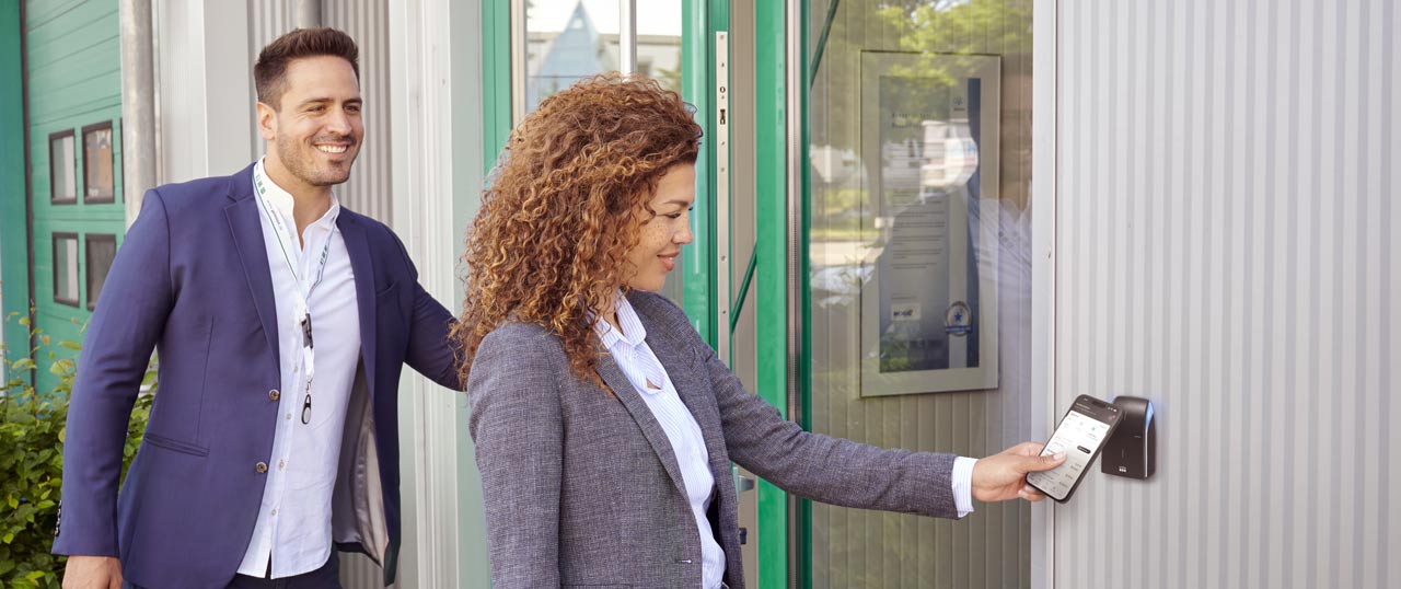 Mujer sostiene el móvil delante de un lector de control de acceso para abrir la puerta.